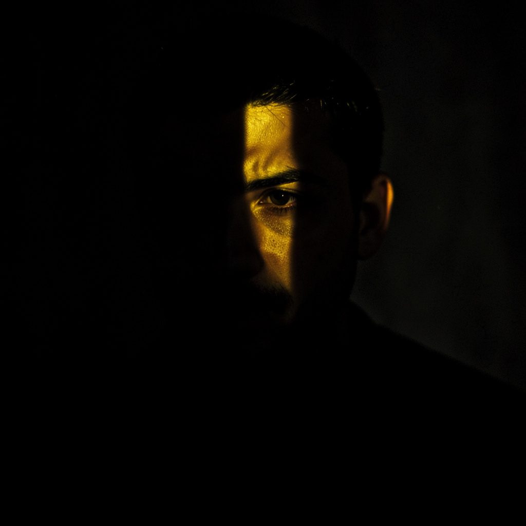 A dark, atmospheric portrait-style still-life suggesting a thoughtful older gentleman's study — worn leather, handwritten notes, and soft amber light against deep shadow.
